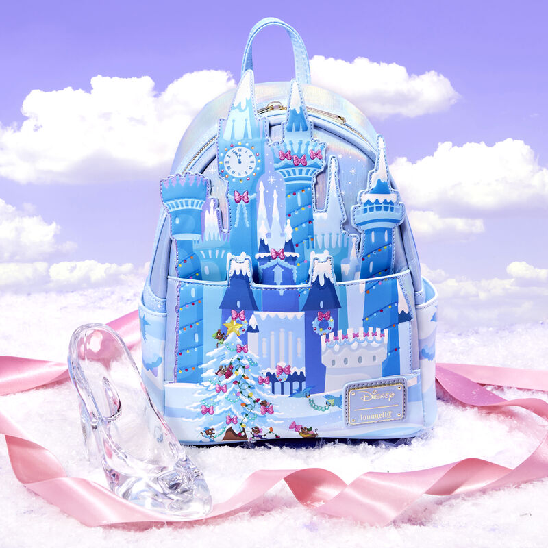 mini backpack against a sky background with a pink ribbon and glass slipper featuring Cinderella's castle decorated for the holidays 